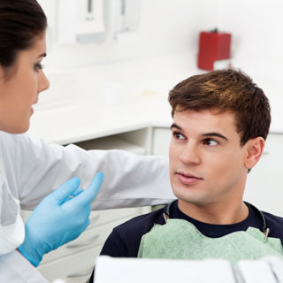 Dentist in blue gloves examining young male patient in modern dental office.