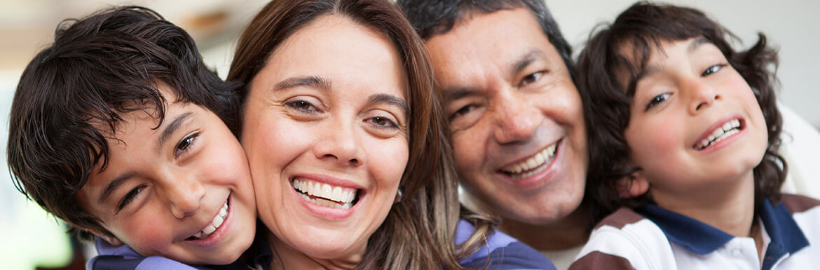 Happy family of four smiling together in close embrace, portraying warmth and dental care trust.