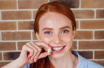 Young woman with red hair smiling at camera against brick wall background.