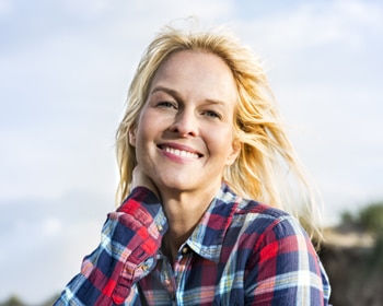 Smiling woman in red plaid shirt outdoors with cloudy sky background
