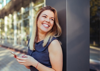 Woman smiling while holding tablet near modern building exterior in urban setting.